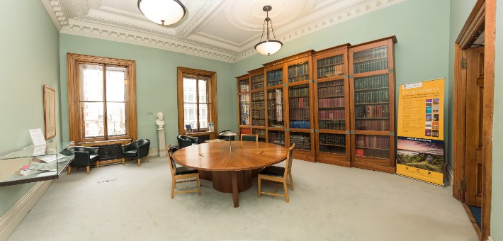 Room with glass cabinets containing books, two sash windows and a circular table with chairs